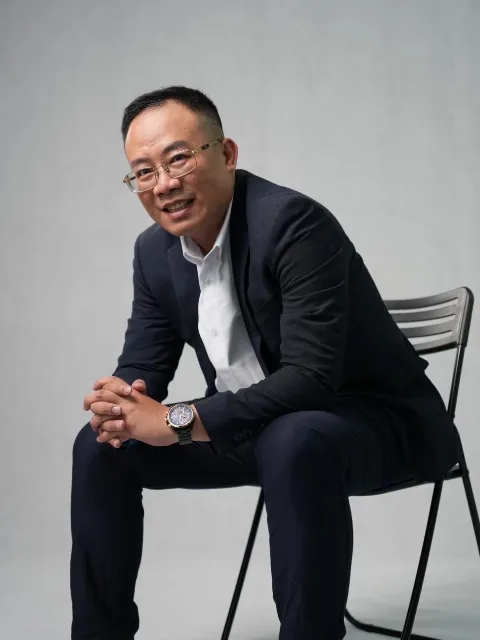 阿生穿著深色西裝，坐在攝影棚的椅子上。